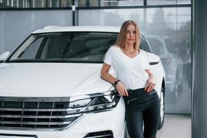 mirando a la cámara. chica y coche moderno en el salón. durante el día en el interior. compra de vehiculo nuevo foto