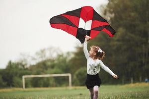 Photo in motion. Happy girl in casual clothes running with kite in the field. Beautiful nature