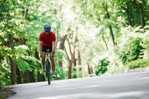 In light clothes. Cyclist on a bike is on the asphalt road in the forest at sunny day photo