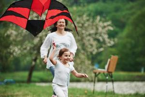 Happiness is in simple things. Positive female child and grandmother running with red and black colored kite in hands outdoors photo