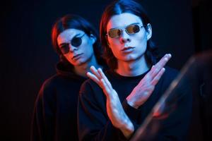 mostrando un gesto que significa detenerse o no hacerlo. retrato de hermanos gemelos. foto de estudio en estudio oscuro con luz de neón