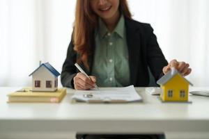 Asian business woman signs contract behind home architectural model - Real estate concept photo