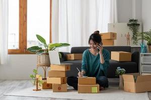 Entrepreneurs Small Business SME Independent woman work at home use smartphones and laptops for commercial checking, online marketing, packing boxes, SME sellers, concept, e-commerce team photo