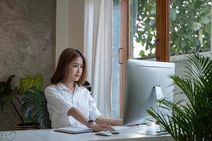 Thinking about business. Thoughtful young  woman looking at computer screen while sitting at his working place at home. Working remotely. photo