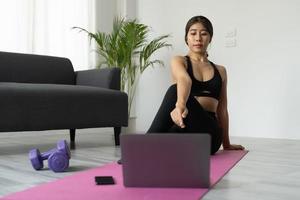 Fit sporty young asian woman online workout exercise at home. Active healthy girl enjoy sport pilates yoga fitness training on laptop computer stretching on yoga mat watching video class photo