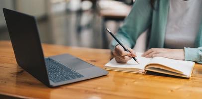 Cropped photo of woman writing making list taking notes in notepad working or learning on laptop indoors- educational course or training, seminar, education online concept