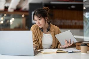 Smiling Asian young female using headset looking at laptop screen listen and learning online courses. Happy business woman with headphones video call for customer service photo