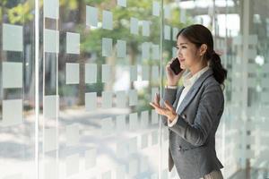 Smiling business asian woman in talking consultant on mobile phone at modern office photo