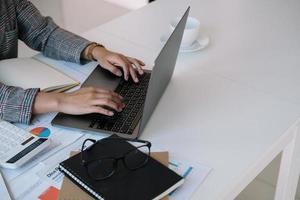 Close up businesswoman using laptop, typing on keyboard with documents, writing email, accountant writing financial report, busy student studying online, searching information. photo