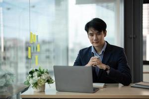 Young asian businessman smiling while working with laptop computer at office, business office concept photo