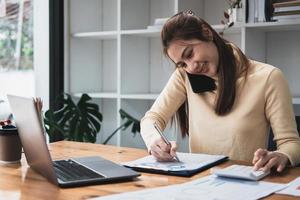 Asian business woman making a phone call, Accountant working Financial investment on calculator with calculate Analyze business and market growth on financial document data graph and writing. photo