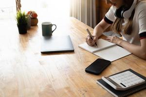 Close up of female hand taking notes in a book with laptop on table. Student studying at home. photo