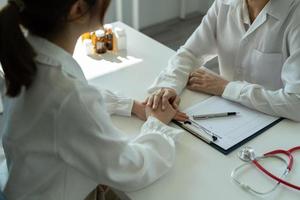 una doctora asiática con uniforme médico blanco consulta a una paciente en un hospital privado. mujer terapeuta habla con mujer cliente en consulta en clínica foto