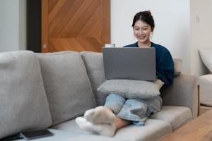 Happy young woman in a blue sweatshirt works at home on a blue sofa with a laptop and a cat, remote work and education, staying at home photo