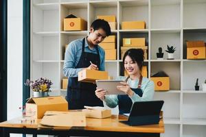 Asian couple doing online business together at home. Helping to pack products into cardboard boxes. family concept, modern business, small entrepreneurs, online delivery photo