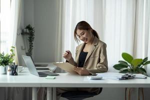 Young asian business woman checks charts and refreshes financial progress. Accountant female analyzes the business model in the workplace. photo