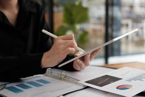 Close up hand of business woman using pen stylus with digital tablet for financial accounting from paperwork chart graph photo