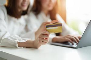 Two asian girlfriends shopping online with laptop computer and credit card at home photo