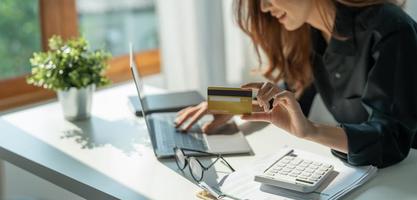 Close up of girl hold bank credit card and type on laptop, shopping online using computer, buying goods or ordering online, entering bank accounts and details in online banking offer. photo