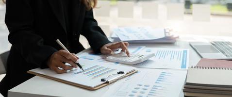 Close up of businessman or accountant hand holding pen working on calculator and laptop computer to calculate business data during make note at notepad, accountancy document at office photo