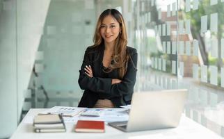 retrata a una mujer de negocios asiática con los brazos cruzados mirando la cámara trabajando con una computadora portátil para la contabilidad financiera en la oficina. foto