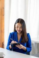 Portrait of a happy asian businesswoman using pen for taking note on notepad at home office photo