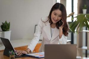 Young business asian woman working on laptop while calling consult by phone in office. photo