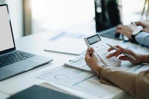 mano de contadora empresaria trabajando en la calculadora para calcular el informe de datos financieros, el documento de contabilidad y la computadora portátil en la oficina, el concepto de negocio foto