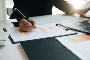 Close up of businesswoman holding a pen and pointing at the information sheet on his desk, reading the company's financials to make a financial plan. Financial concept. photo