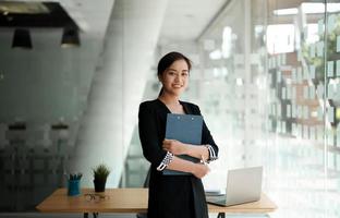 Retrato mujer asiática de negocios de confianza de pie mientras trabaja para la contabilidad financiera con una computadora portátil y una calculadora foto