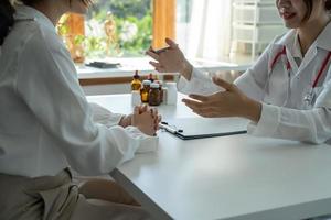 una doctora asiática con uniforme médico blanco consulta a una paciente en un hospital privado. mujer terapeuta habla con mujer cliente en consulta en clínica foto