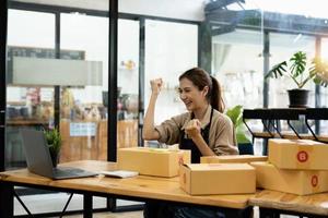 Happy young Asian woman entrepreneur, Smile for sales success after checking order from online shopping store in a smartphone at home office, Concept of merchant business online and eCommerce photo