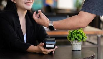 Cropped image of Businessman making a payment by using a smart watch with blurred cafe restaurant as background. NFC technology concept photo