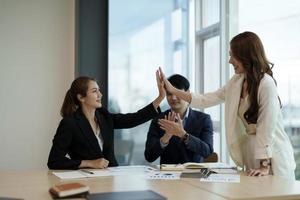 Diverse asian business team celebrating and giving high fives during boardroom meeting. business financial concept photo