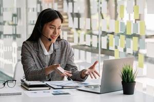 Asian woman in wearing headphones, enjoying watching educational webinar on laptop. Smiling young mixed race businessman holding video call with clients partners. photo