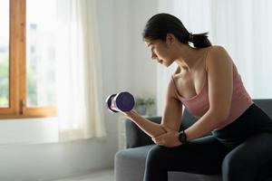 concepto de entrenamiento en casa mujer asiática en la sala de estar con levantamiento de pesas salud mental en cuarentena foto