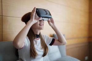 excitar a una mujer asiática jugando juegos en línea con gafas vr y controlador en su casa foto