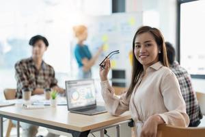 grupo de jóvenes empresarios asiáticos con ropa informal inteligente trabajando juntos en una oficina creativa usando una laptop. foto