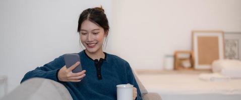 feliz joven asiática usando teléfono móvil mientras se sienta en un sofá en casa foto