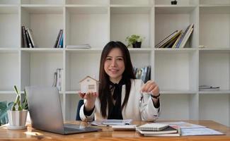 retrato asiático empresaria bienes raíces mano sosteniendo casa modelo y clave, concepto de corredor de venta de casa. foto