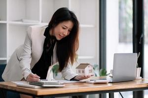 Charming asian woman holding house model in hand and calculating financial chart for investment to buying property. photo