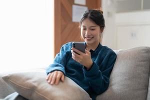 feliz casual hermosa mujer asiática está hablando por teléfono sentado en un sofá en casa. foto