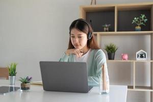 Concentrate asian gial freelancer wearing headset, communicating with client via video computer call. Millennial pleasant professional female tutor giving online language class. photo