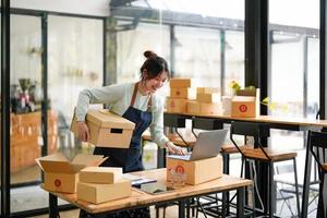 Startup small business SME, Entrepreneur owner using laptop computer taking receive and checking online purchase shopping order to preparing pack product box. Selling online ideas concept photo