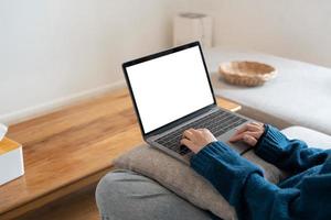 Top view mockup image of a woman working and typing on laptop computer with blank screen while sitting on a sofa at home photo