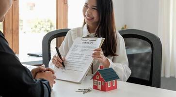 Real estate brokers point to a contract paper and advise customers to sign their names. customer sign agreement contract signature for buy or sell house. Real estate concept contact agreement concept photo