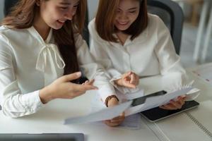 Two colleagues or students, asian girl working for financial paperwork while sitting at workplace discussing about job or education photo