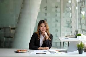 Portrait of attractive business woman sitting at her desk with laptop computer in office. Smiling business woman in black suit at office photo