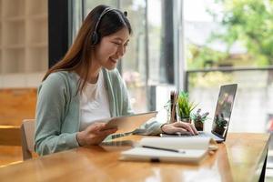 mujer asiática escribiendo haciendo una lista tomando notas en el bloc de notas y la tableta digital trabajando o aprendiendo en una computadora portátil en el interior: curso educativo o capacitación, seminario, concepto de educación en línea foto