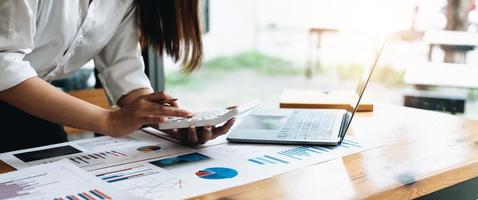 Cerca de la mano del empresario o contador sosteniendo un lápiz trabajando en la calculadora para calcular el informe de datos financieros, el documento de contabilidad y la computadora portátil en la oficina, concepto de negocio foto